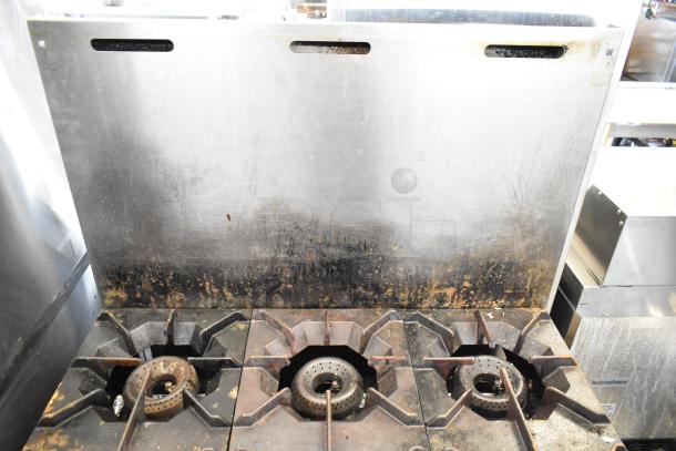 American Range commercial 6 burner gas stove with oven and backsplash. Visible wear and discoloration on the burners.