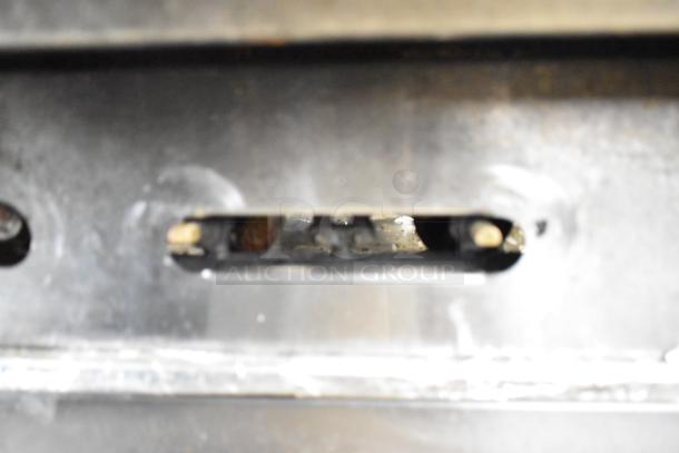 Close-up of a part from an American Range commercial gas-powered 6-burner range, showing metal components.