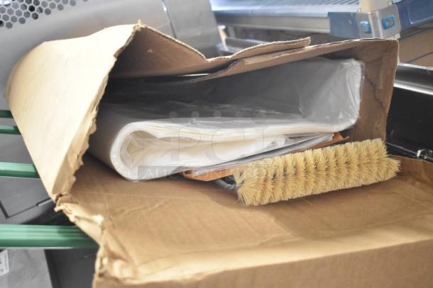 Cardboard box containing a wrapped stack of papers and a cleaning brush, likely packaging materials for the Frymaster fryer.