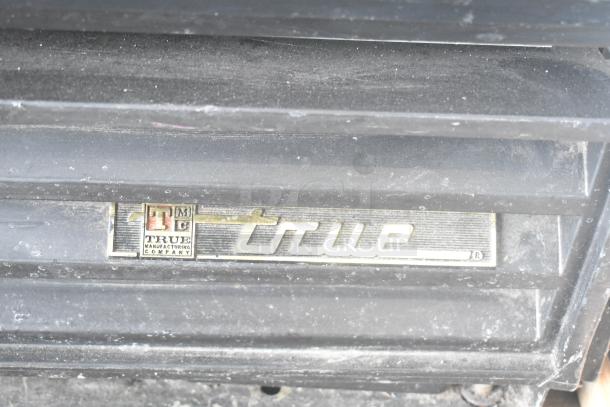 True GDM-12 cooler label, highlighting brand and model on black surface. Dust visible, indicating used condition.