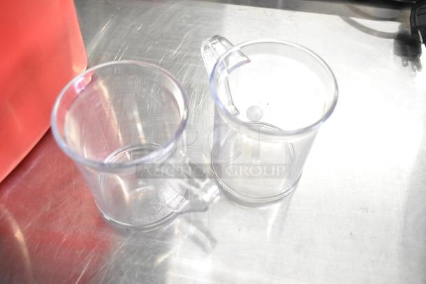 Clear poly pitchers with handles beside a red poly bucket on a metal surface. Auction lot includes 10 assorted items.
