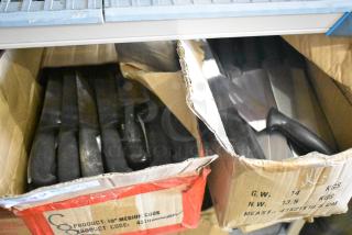 100 sharpened stainless steel knives, including chef knives, in open boxes. Black handles, product codes visible.
