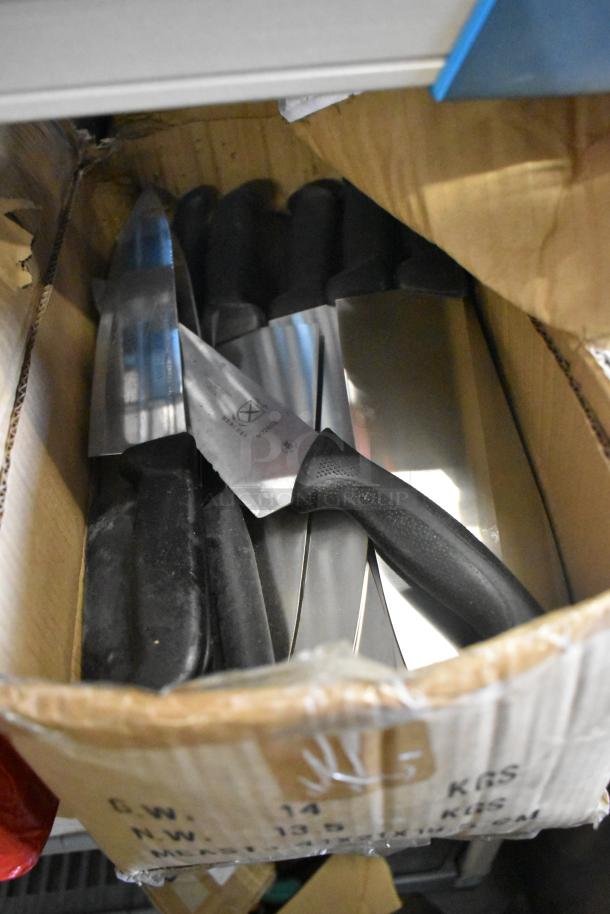 Box of 100 sharpened stainless steel knives, including chef knife, visible with black handles, packed in cardboard box.