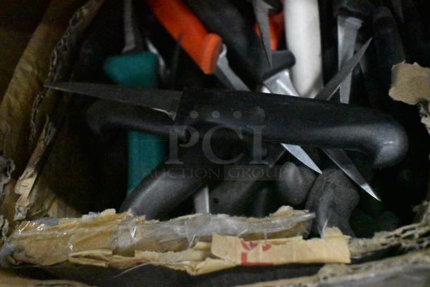 Box of assorted sharpened stainless steel knives, including poultry and paring knives. Various colors, black handles visible.