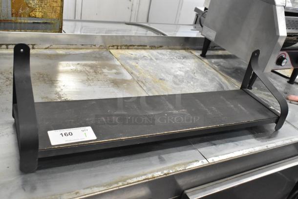 Black metal wall mount shelf with curved supports, showing slight wear; auction tag reading "160, QTY 1" visible.