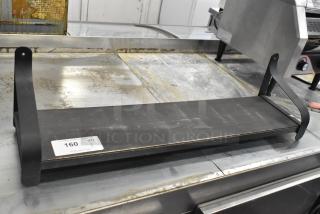 Black metal wall mount shelf with curved supports, showing slight wear; auction tag reading "160, QTY 1" visible.