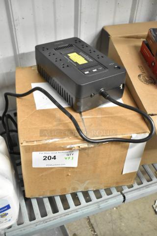 Alt text: Uninterruptible power supply on cardboard box with visible cable, part of auction lot including office telephone. Box labeled "204 QTY X3."