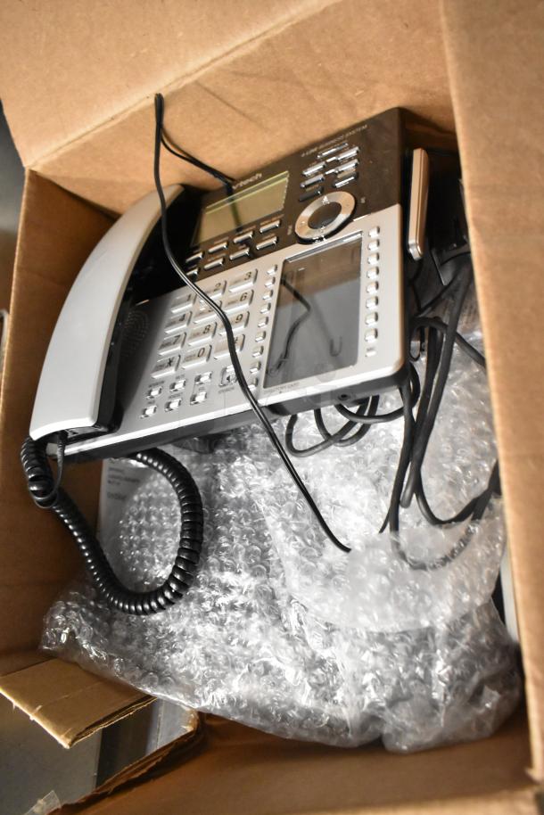 Cardboard box containing a corded office telephone with keypad and display, wires, and bubble wrap cushioning.