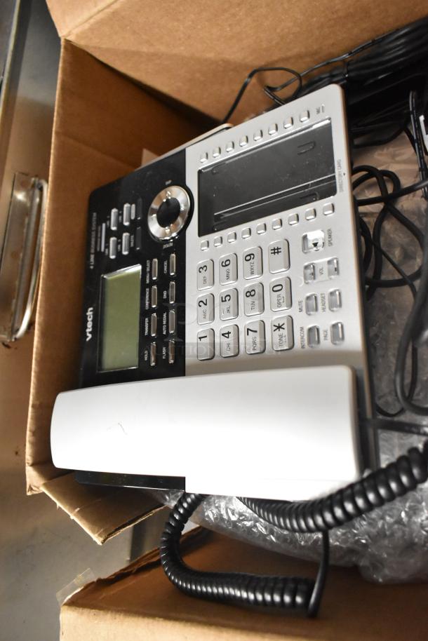 VTech corded office phone in a cardboard box, visible buttons, and display screen, bundled cords. Good condition.