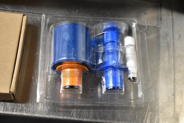 Three items: 2 HT03XL-BTI Li Polymer Batteries and Fargo DTC Color Ribbon in packaging on a silver surface.