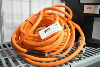 Coiled orange propane gas hose with metal fittings, auction tag shows item 208, quantity x2, on metal shelf.