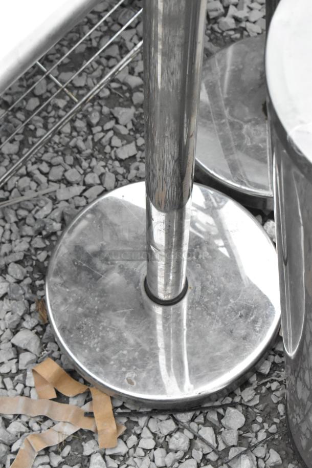 Shiny metal stanchion base on gravel, part of a set including a trash can and another stanchion. Auction item, used condition.