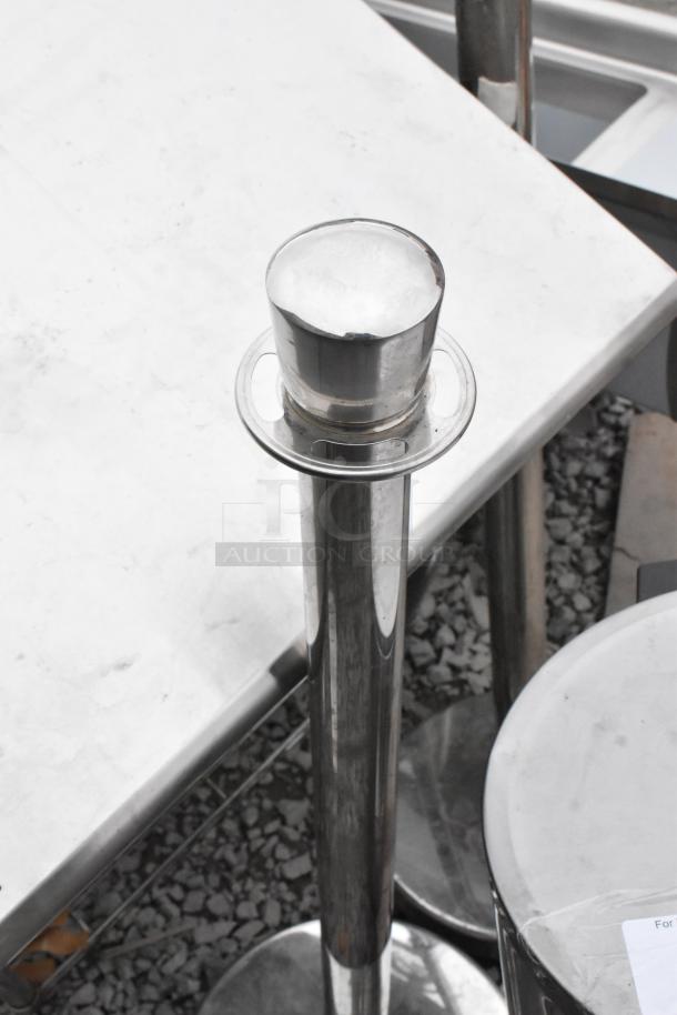 Chrome stanchions and cylindrical trash can on gravel, indicating used condition. Ideal for event settings.