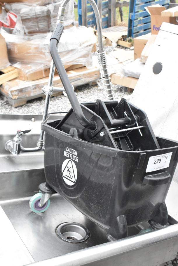 Black poly mop bucket with wringing attachment, "Caution Wet Floor" label, auction tag #220, used condition.