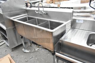 Commercial 3 bay stainless steel sink with faucet and handles, used condition, includes side drainboard.