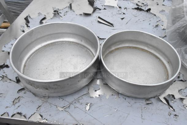 Two round metal baking pans in used condition, with visible scratches. Auction includes 49 pans total.