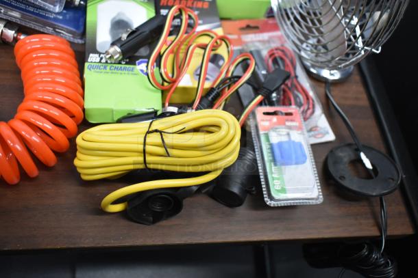 Assorted electronics including a fan, USB chargers, adapters, strobe light, headlamp, and duster gun on a table.