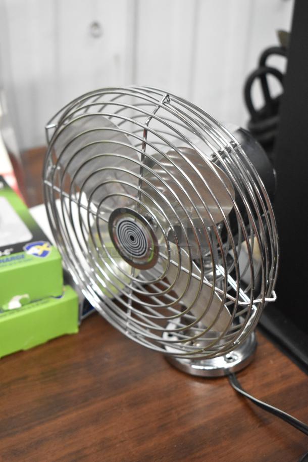 Table fan with metal grille, part of a 25-item auction lot, including chargers, adapters, and lighting accessories.