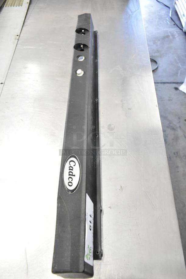 Brand new Cadco part, shown atop metal surface. Includes logo and item label. Ideal for replacement or spare.