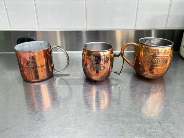 Assorted copper Moscow Mule mugs by Commercial Barware, featuring hammered copper and stainless steel, with visible branding.