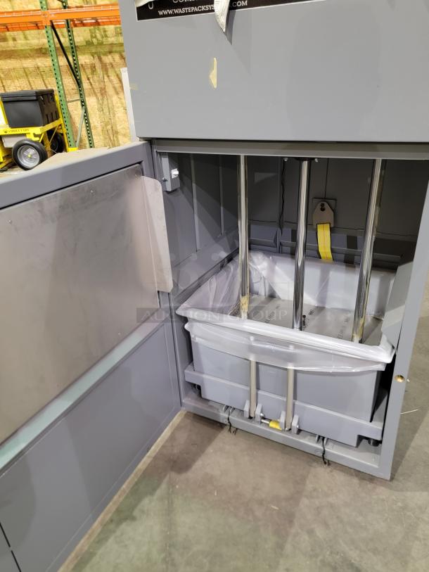 Fox Compactors 2430 industrial waste compactor with bin on casters, gray steel frame, open door showing compacting mechanism.