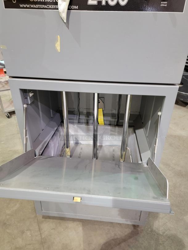 Fox Compactors 2430 industrial waste compactor with two-dial control, steel frame, and bin on casters. Model branding visible.