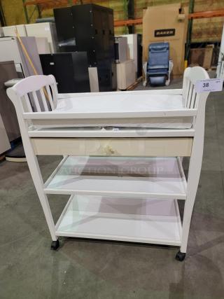 White Sorelle Manhattan changing table with padded top, star knob drawer, two shelves, and casters for easy mobility.