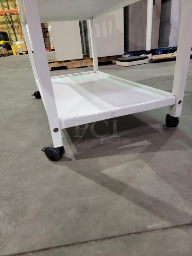 White Sorelle Manhattan changing table with two shelves, star-shaped knob, and wheels for easy mobility, shown on a warehouse floor.