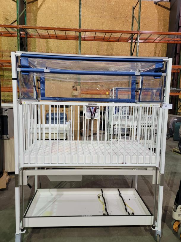 Novum E1982CGT pediatric crib, durable manual crank system, safety side-gate, high-quality swivel casters, storage tray included.