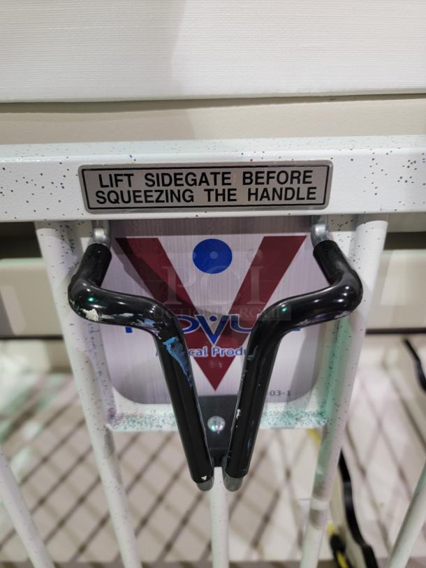 Novem E1982CGT pediatric crib with side-gate label, manual crank, durable casters, and base storage; professional condition.