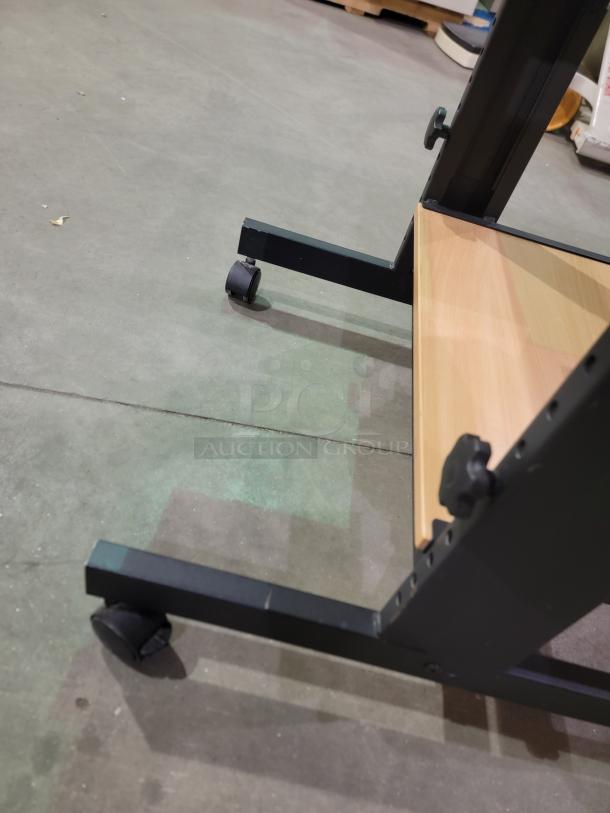 Mobile computer cart with black metal frame, heavy-duty casters, and wood shelf; ideal for workspace efficiency and mobility.
