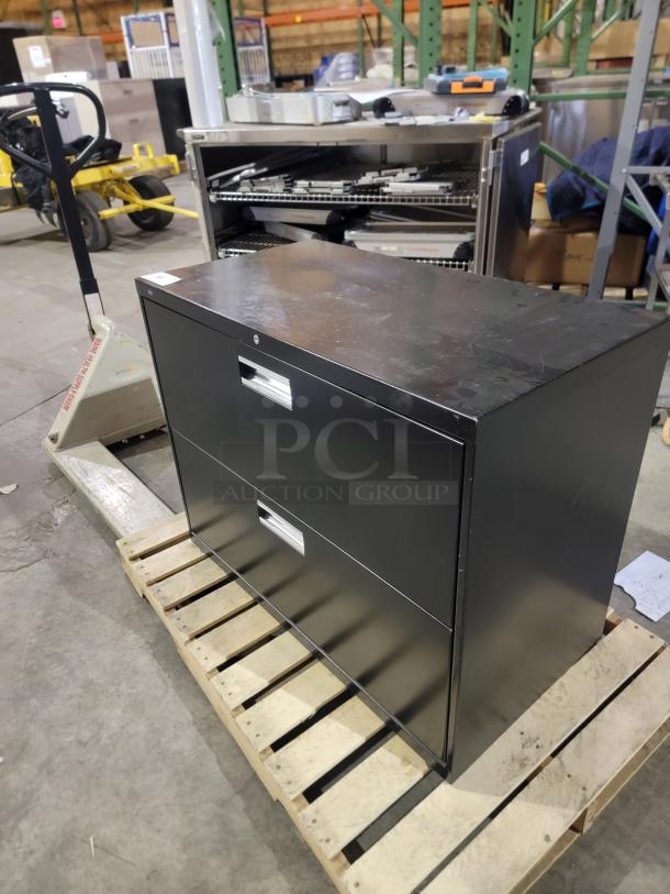 Hon Brigade 600 Series 2-drawer lateral file, black, heavy-duty steel, extra-wide drawers on a pallet, in a warehouse setting.