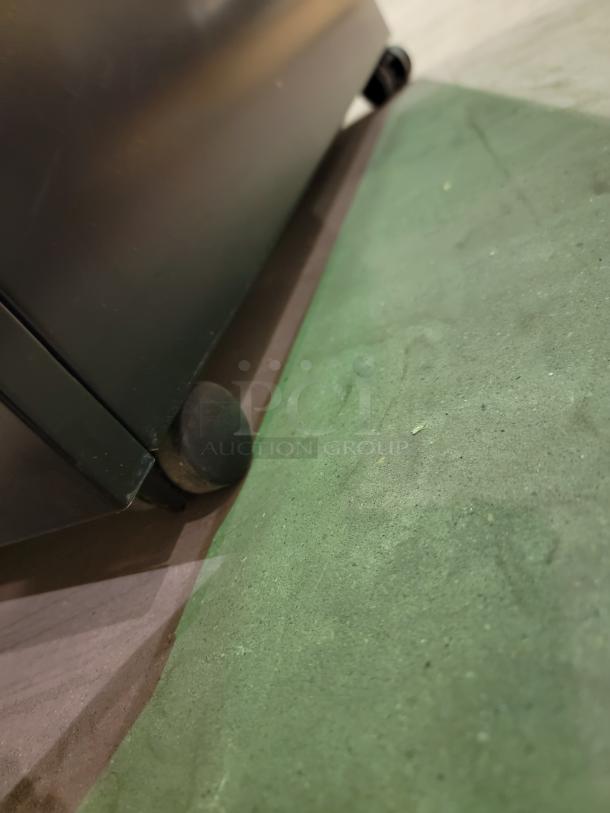 HP M2705A mobile storage unit close-up showing smooth-rolling caster. Black steel chassis. Professional-grade versatility.