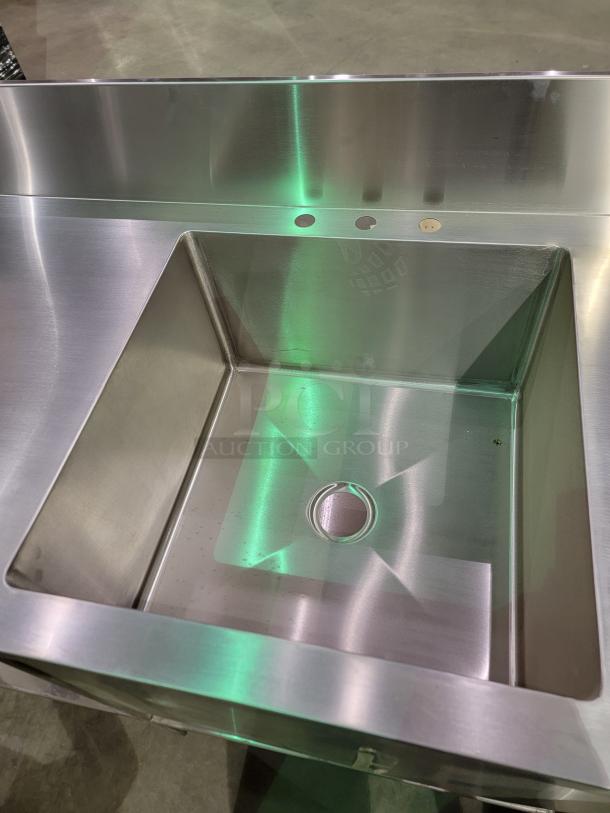 Heavy-duty stainless steel prep table with 24-inch deep bowl sink, backsplash, and undershelf, ideal for commercial use.