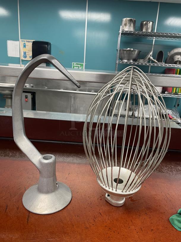 Hobart H-600 mixer attachments: a heavy-duty dough hook and wire whip on a wooden surface, showcasing durability.