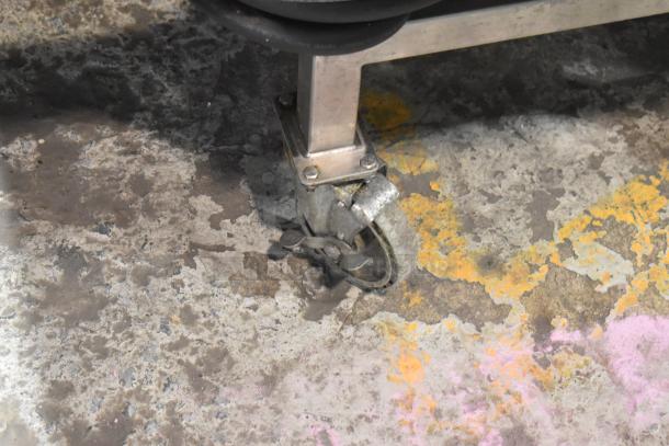 Close-up of a metal caster wheel on a Turbochef HhC2020 oven stand, showing wear on a concrete floor.