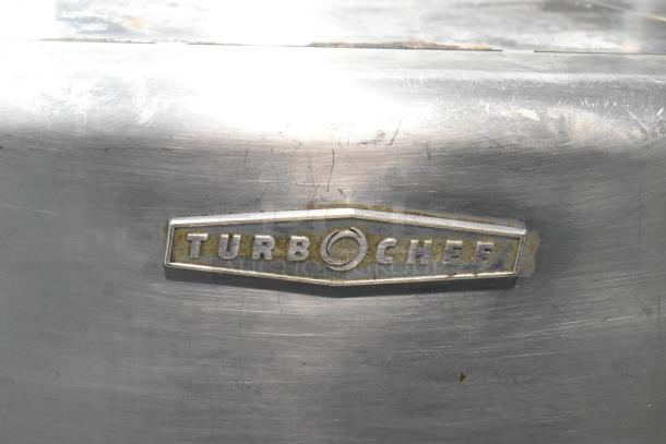 Close-up of a Turbochef HhC2020 commercial oven's metal surface with the brand logo. Surface shows wear marks.