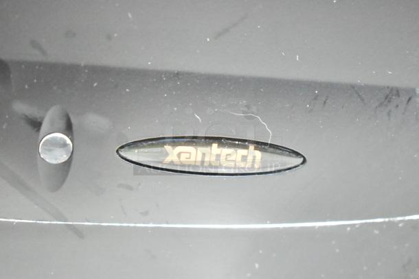 Close-up of Xantech logo on a black electronic device, likely a component video switcher. Surface shows minor wear.