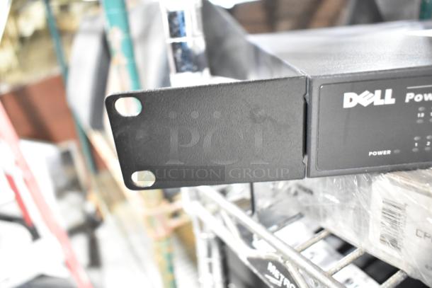 Dell PowerConnect 2024 switch on metal shelving, visible front panel with power button, part of auction lot.