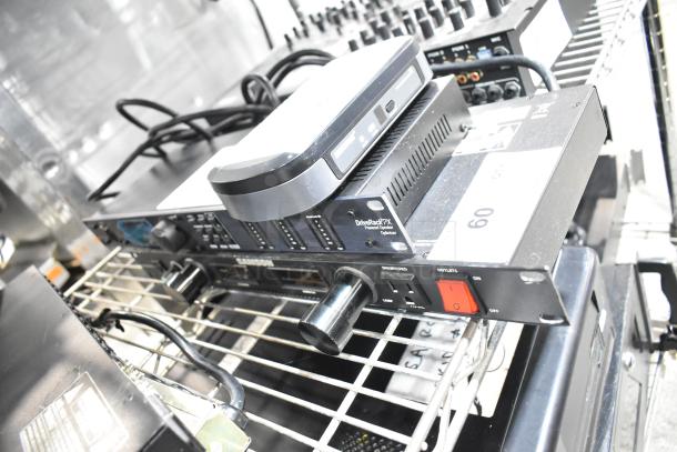 Shure PG4, DBX DriveRack PX, and Samson PowerBrite Pro15 audio devices on shelf, showing inputs, knobs, and power switch.