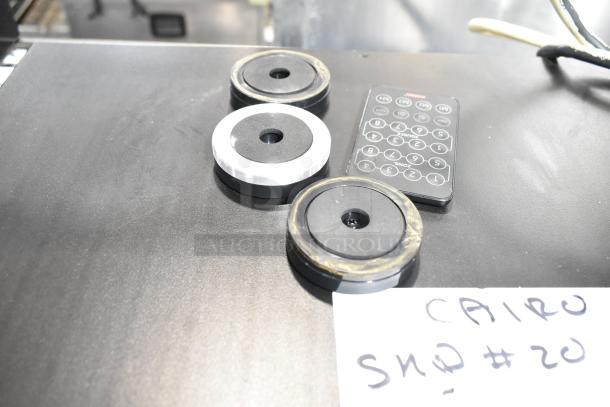 Circular weights and remote control on black surface, near handwritten note "CAIRO SND #20."
