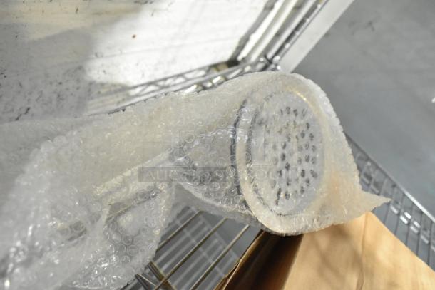 Brand new Regency sink drain in bubble wrap, visible scratches and dents, metal finish, unused condition.