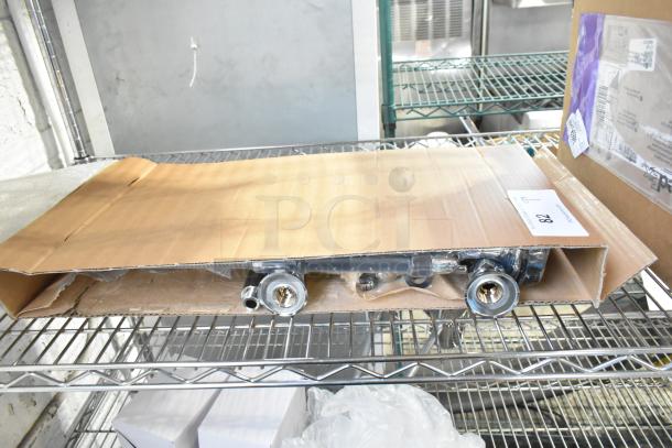 Brand new spray nozzle attachment with scratches and dents, partially visible in an open cardboard box on metal shelving.