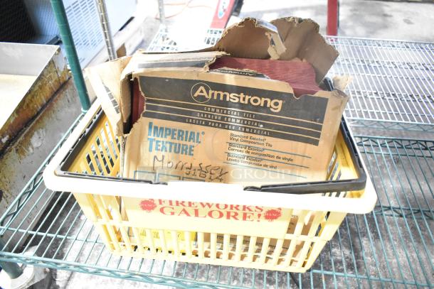Yellow basket containing mixed items, including an Armstrong Imperial Texture tile box. Signs of wear on cardboard.