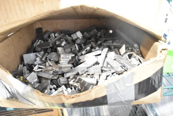 Cardboard box filled with assorted metal parts, some labeled with measurements, likely for hardware use. Condition appears used.