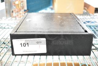 Black metal box with textured finish, labeled "101" by PCI Auctions, in used condition and resting on a wire shelf.