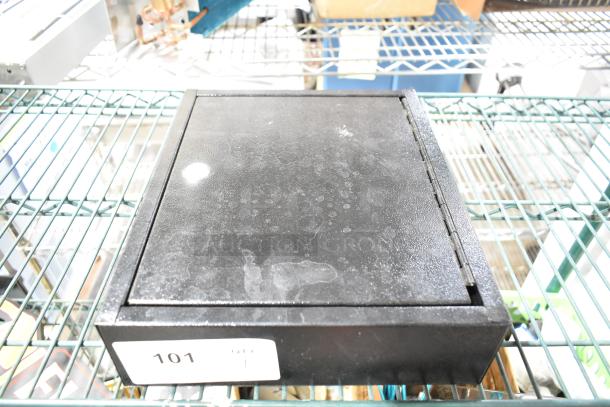 Black metal box with hinged lid, shows wear and scuff marks. Label reads "101." Rectangular shape, sturdy design.