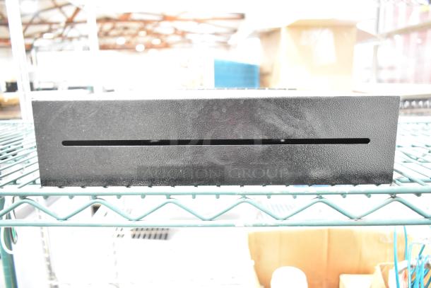 Black metal box with a slot on top, textured finish, in good condition, placed on wire shelving.