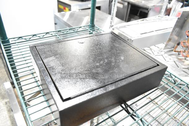 Black metal box with textured surface on wire shelf, showing minor wear. Likely used for storage or security purposes.