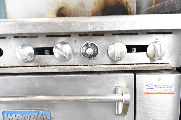 Imperial commercial gas range with 4 burners, flat top griddle, oven, overshelf, and backsplash. Visible wear, on casters.